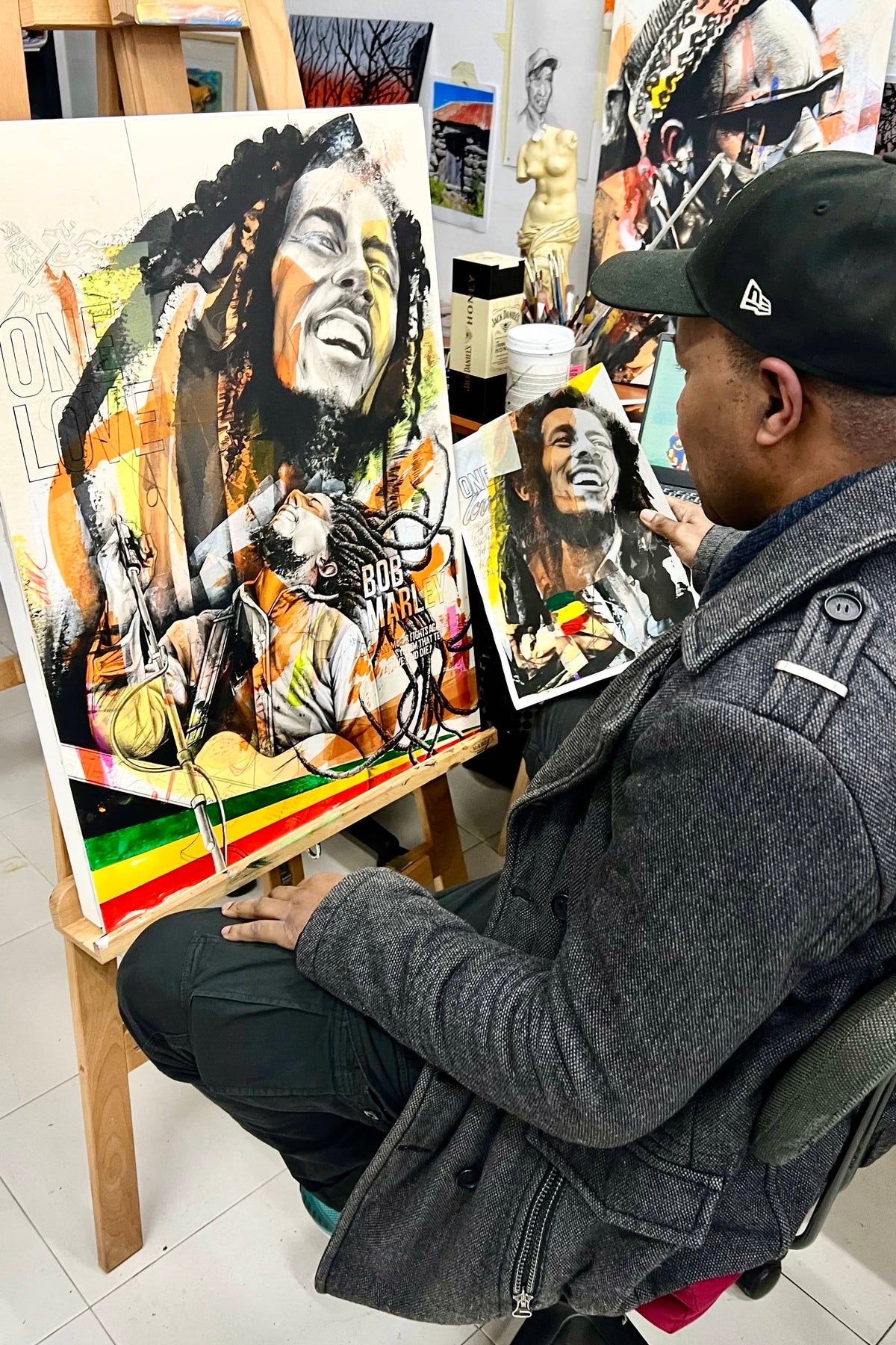 Person sitting in front of a painting of a famous musician, surrounded by art supplies.